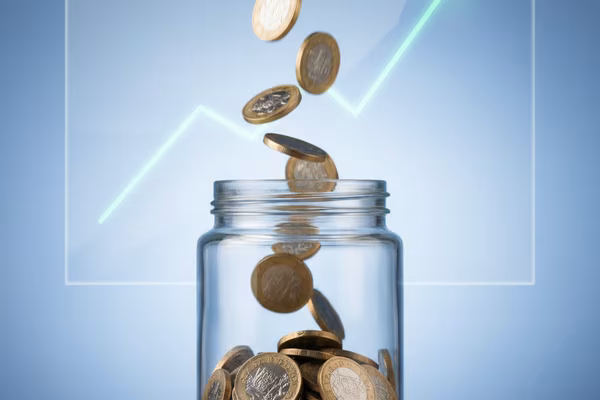 British pound coins falling into a clear glass jar with growth chart in background